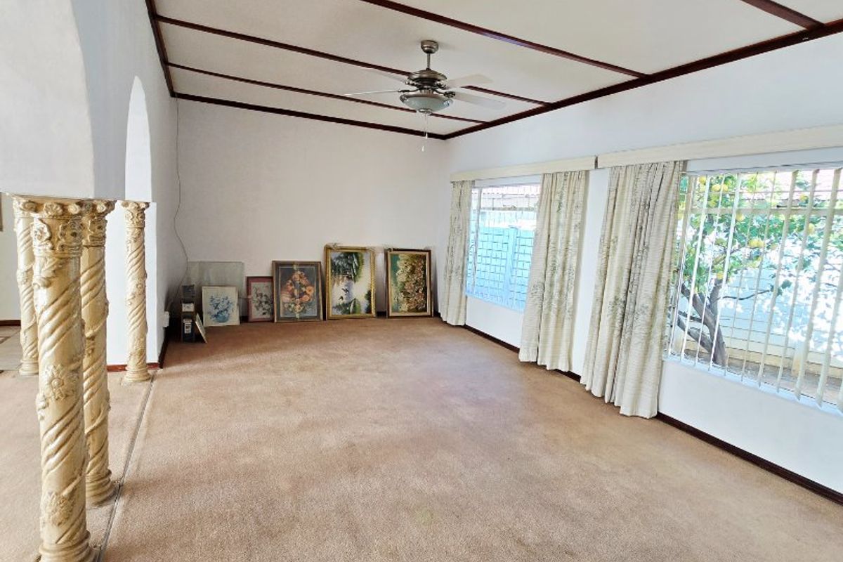 Spacious living room featuring decorative columns, exposed beam ceiling, ceiling fan, and large windows with security bars.