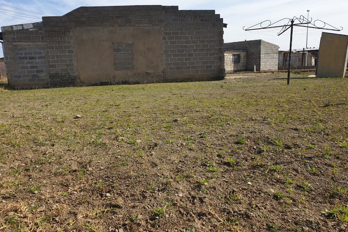 Rear view of the property showing an unplastered brick structure and a large, undeveloped yard area with a rotary clothesline.