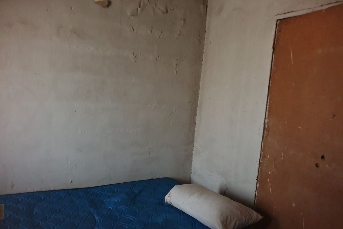 A bedroom space featuring unfinished plaster walls and a worn door, requiring significant renovation and finishing to reach a habitable standard.