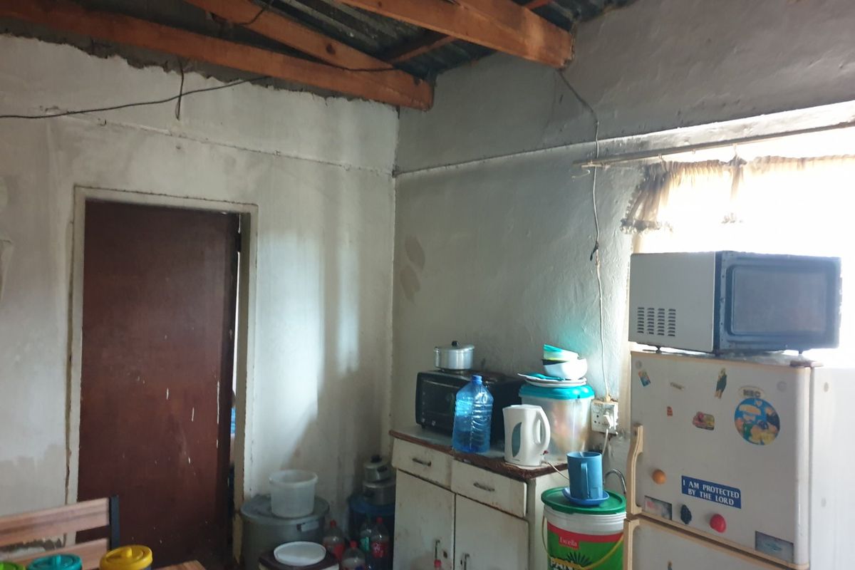 A basic kitchen area featuring exposed timber rafters, corrugated metal ceiling, and simple base cabinetry, requiring significant renovation and finishing.