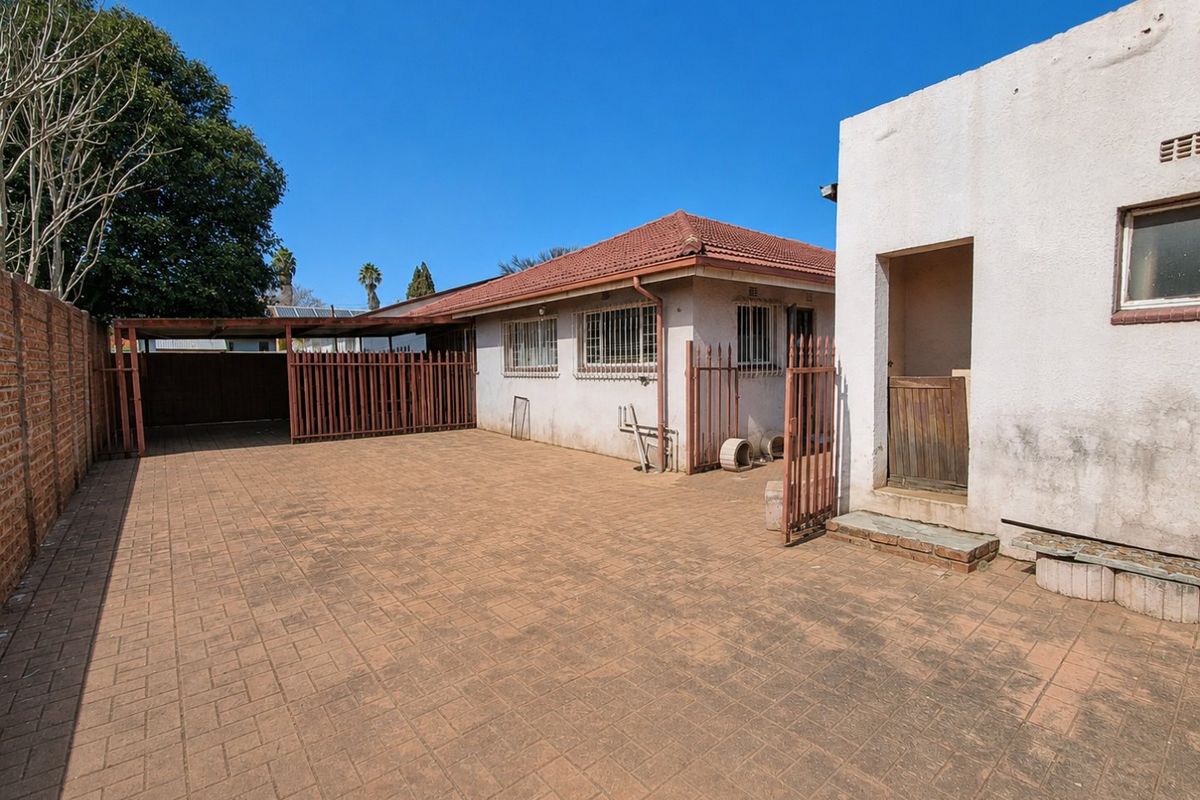 Rear exterior view featuring a paved courtyard, carport, and secure access gates with perimeter brick walling.