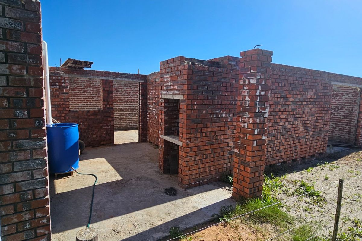 An unfinished exterior structure featuring exposed brick walls, a built-in brick braai, and a concrete slab foundation, currently under construction.