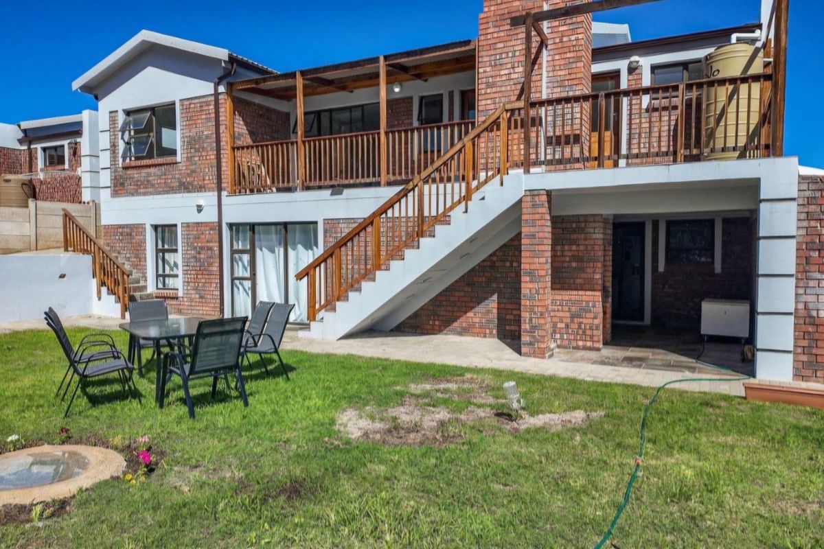 Rear view of a double-story brick house featuring a wooden balcony, external staircase, paved patio area, and a private garden.