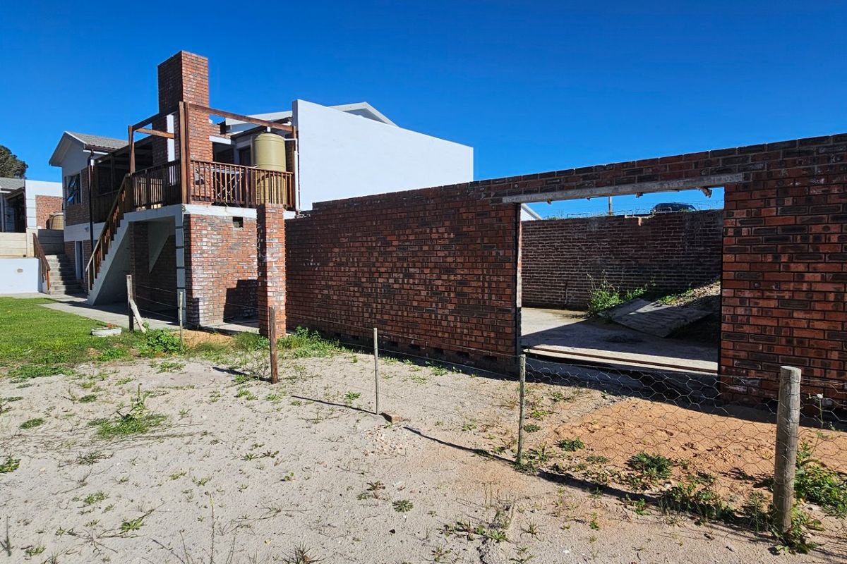 Rear view of the property showing a multi-level structure with a wooden deck, brick chimney, and an unfinished brick boundary wall in the yard.