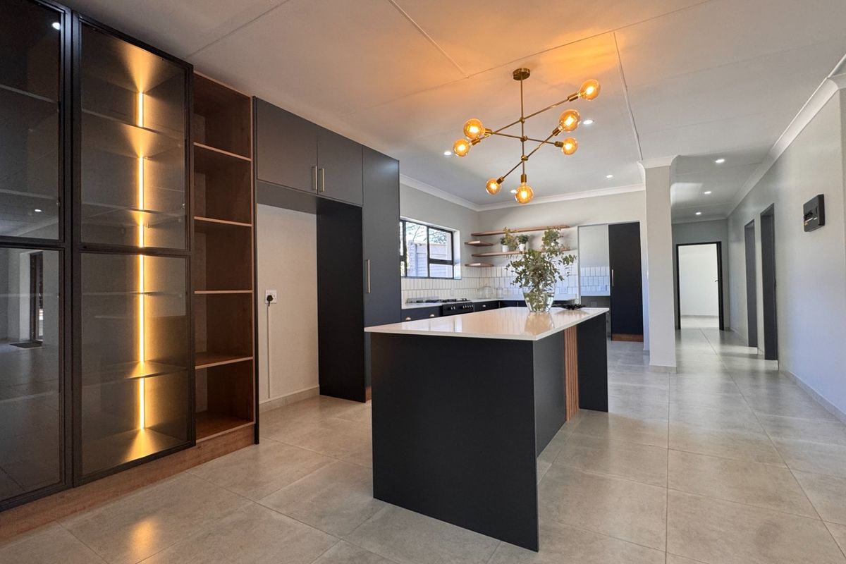 Modern kitchen featuring a central island, sleek dark cabinetry, stone countertops, open shelving, and contemporary pendant lighting in an open-plan layout.