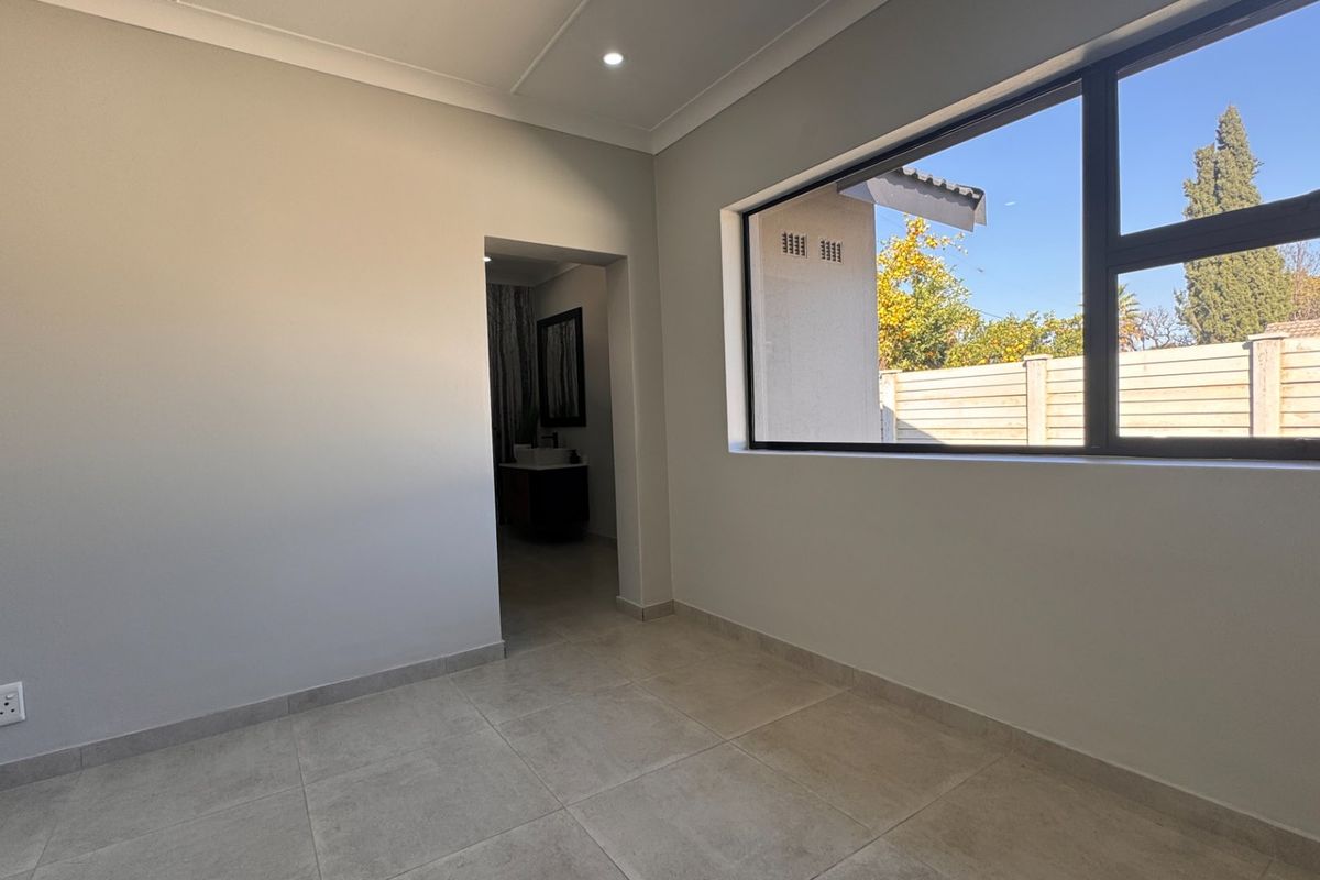 A bright, empty bedroom featuring neutral tiled flooring, recessed downlighting, and a large window providing natural light and views of the rear garden.