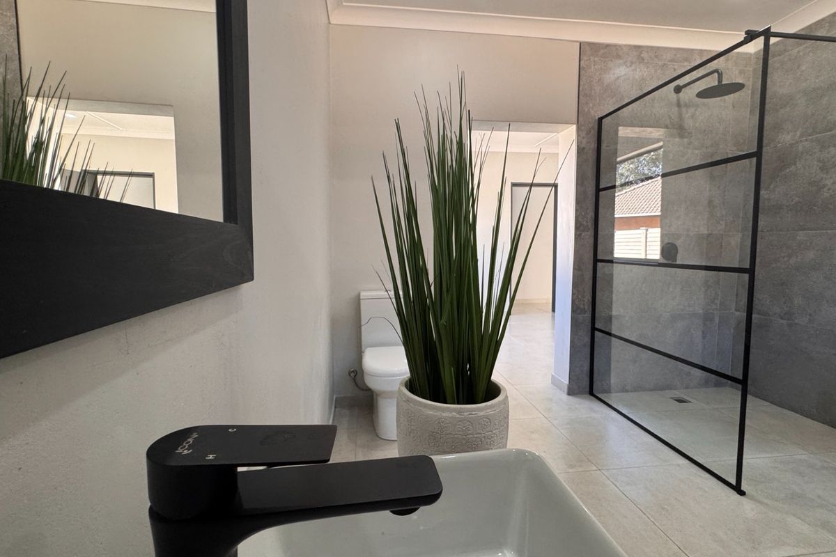 Modern bathroom featuring a walk-in shower with black-framed glass screen, contemporary black tapware, and neutral floor-to-ceiling tiling.