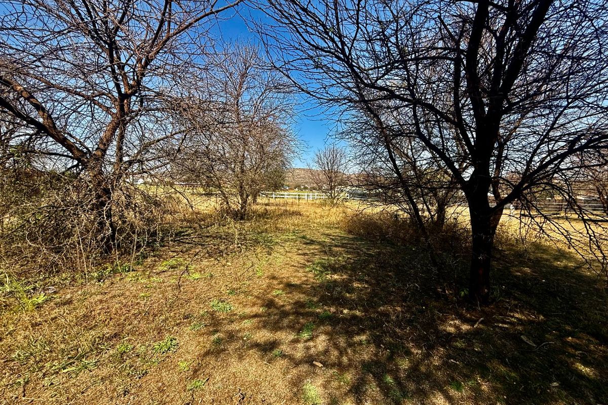 A view of a vacant residential plot featuring mature trees and perimeter fencing, offering a natural landscape setting.