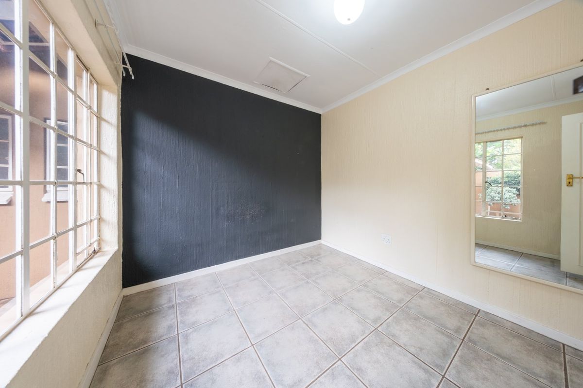 An empty bedroom featuring tiled flooring, a dark accent wall, and security bars on the windows, providing a blank canvas for personalization.