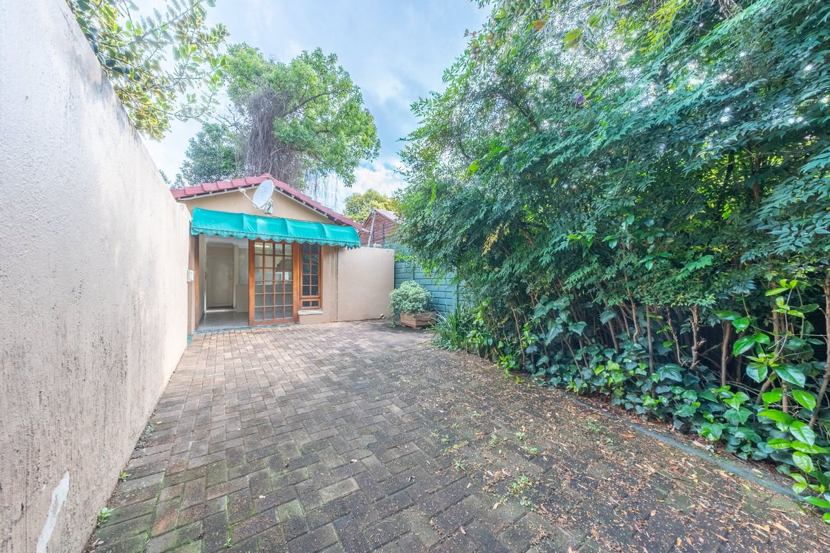 A private rear courtyard featuring paved flooring, a boundary wall, and a timber-framed glass entrance door with a protective awning.