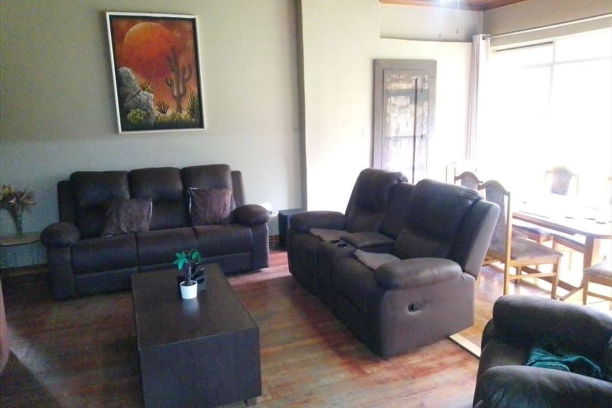 A living room featuring timber ceiling paneling and laminate flooring, offering a functional space with potential for cosmetic updates.