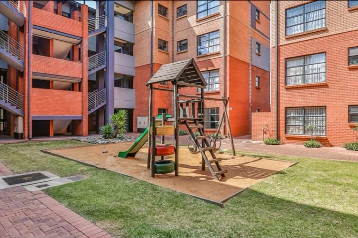 A communal courtyard area within an apartment complex featuring brick building facades, paved pathways, and a children's playground structure.