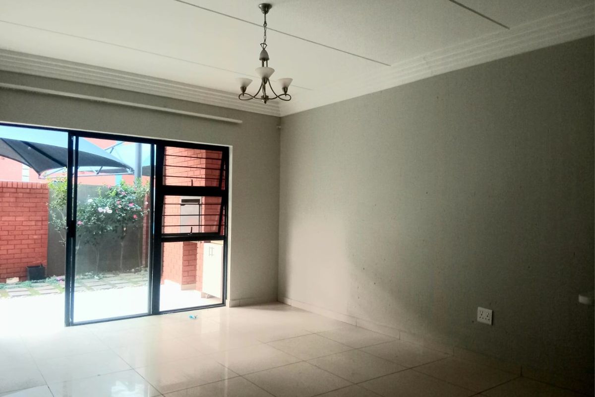 An empty living room featuring tiled flooring, a coved ceiling, and a large sliding glass door providing access to an outdoor patio area.