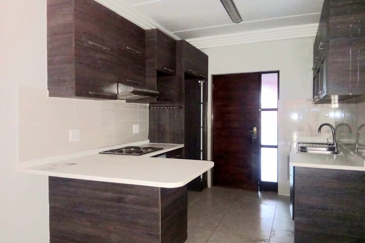 Modern kitchen featuring dark wood-look cabinetry, white countertops, integrated hob with extractor, and tiled flooring in a clean, functional layout.