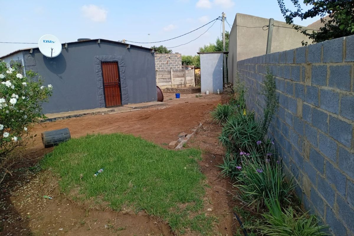 Rear exterior view of the property featuring a concrete block boundary wall, unpaved yard space, and a secondary utility structure.