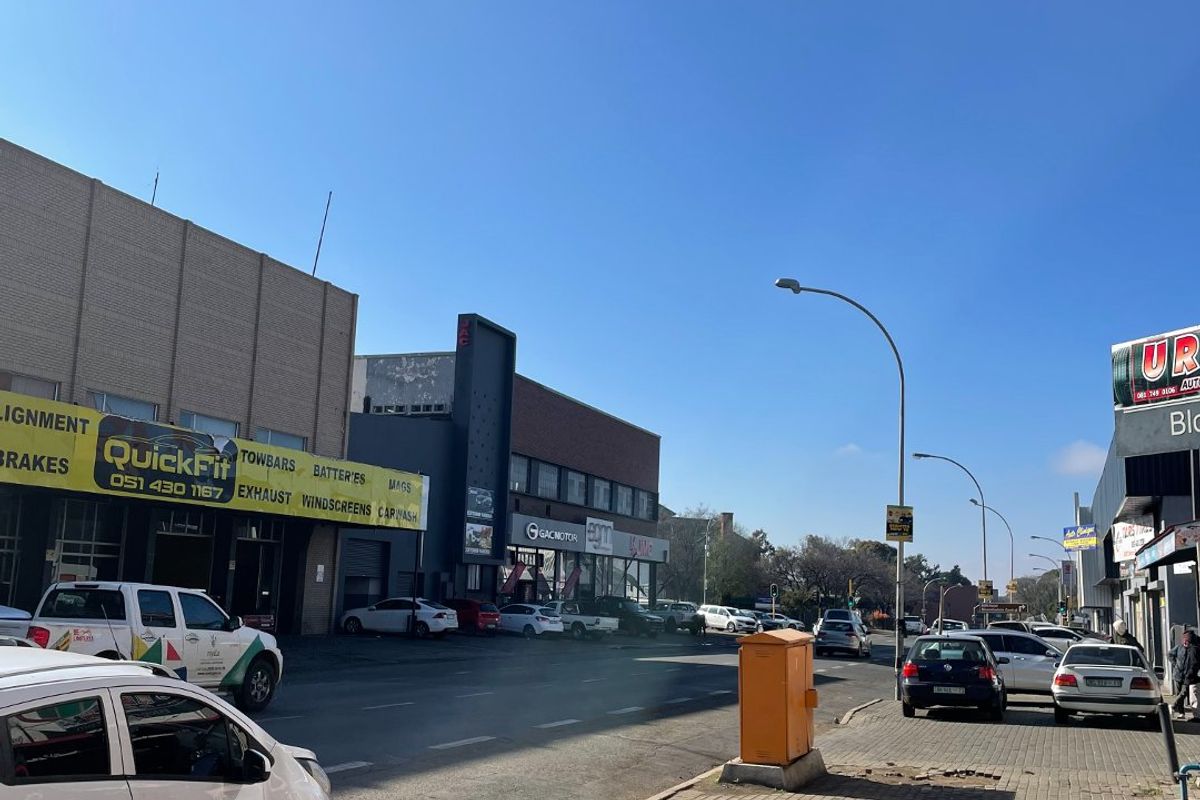 A street-level view of a commercial area featuring paved sidewalks, street lighting, and various automotive service business storefronts along the road.