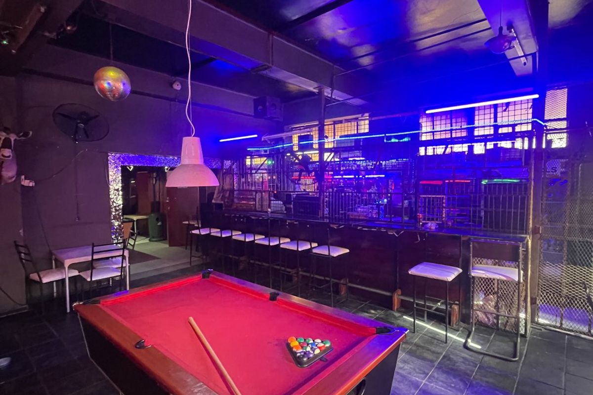 A commercial bar area featuring a built-in counter, tiled flooring, and exposed ceiling structure, illuminated with ambient blue accent lighting.