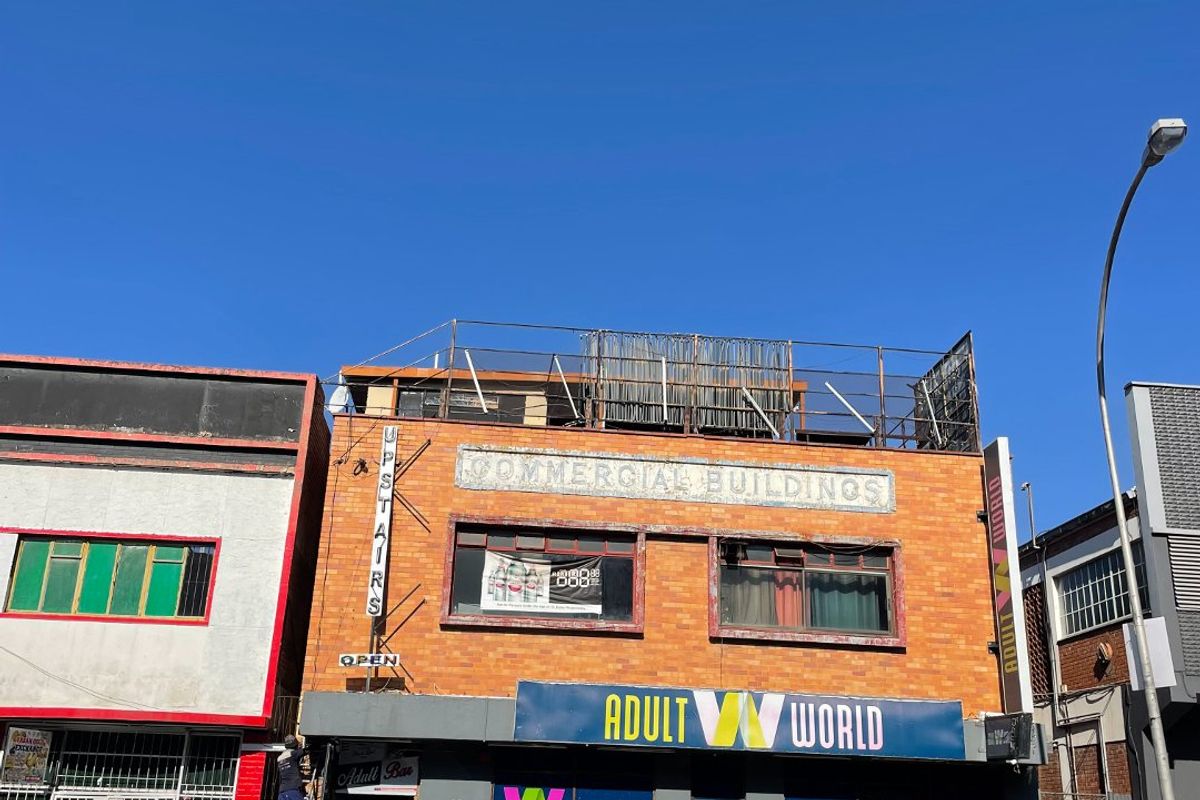 Front elevation of a multi-story commercial building featuring brick facade, prominent signage, and a steel roof structure.