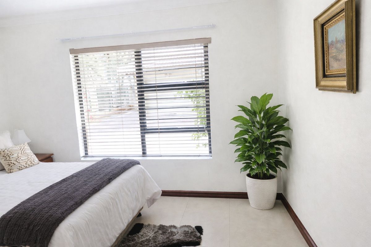 A bright and well-maintained bedroom featuring neutral tiled flooring, clean white walls, and fitted venetian blinds.