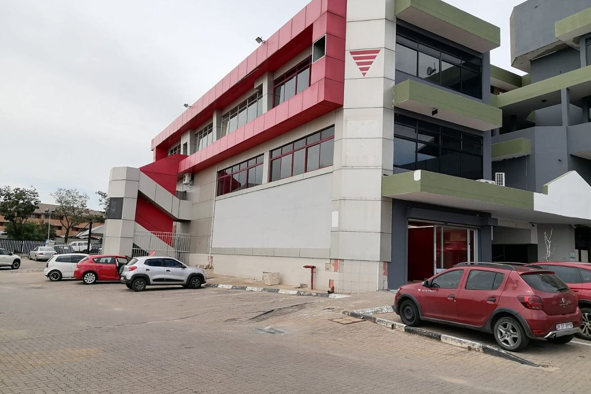 Commercial multi-story building featuring a paved parking area, external staircase, and modern metal cladding facade with tinted windows.
