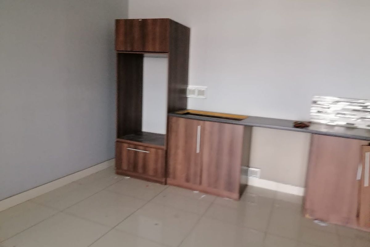 A partially fitted kitchen area featuring dark wood-look cabinetry, a tiled backsplash, and tiled flooring, currently awaiting sink and appliance installation.