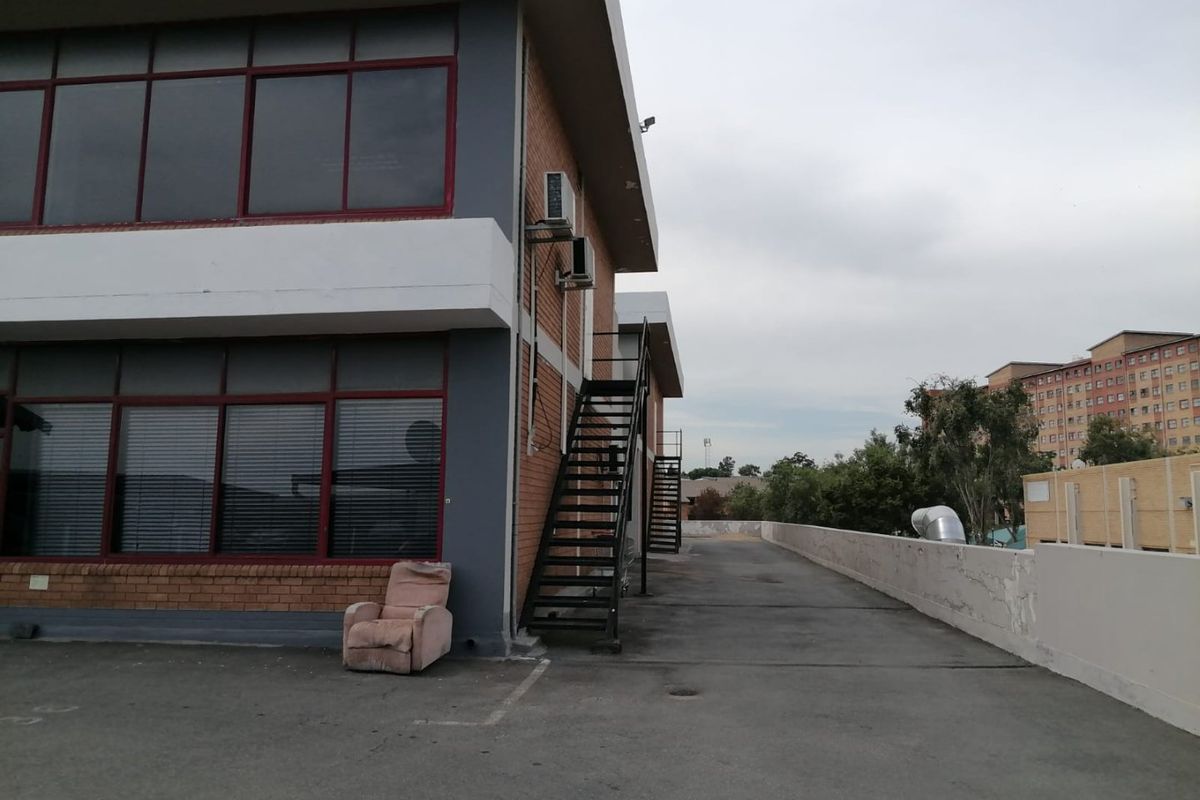 Rear exterior view of a commercial building featuring a metal staircase, brick facade, and paved area with wall-mounted air conditioning units.