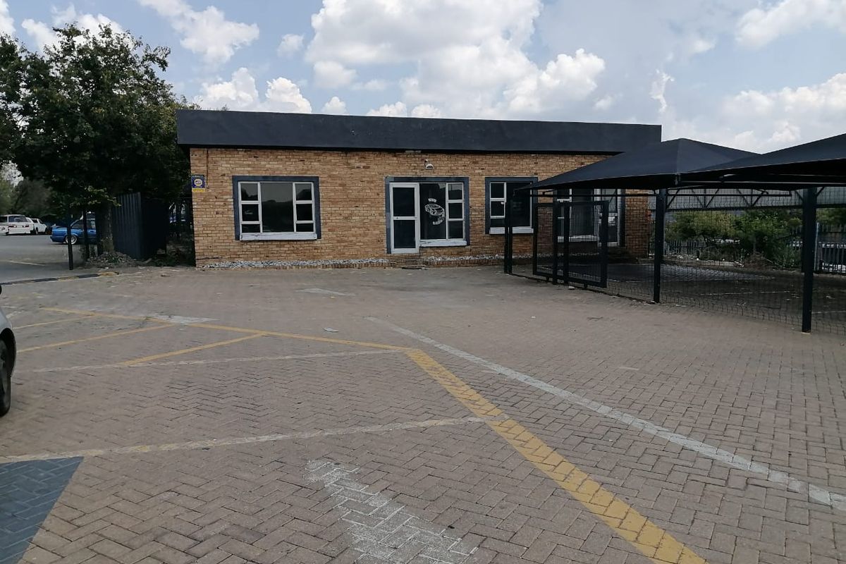 Commercial property exterior featuring a face brick facade, paved parking area, and a shade cloth carport structure.
