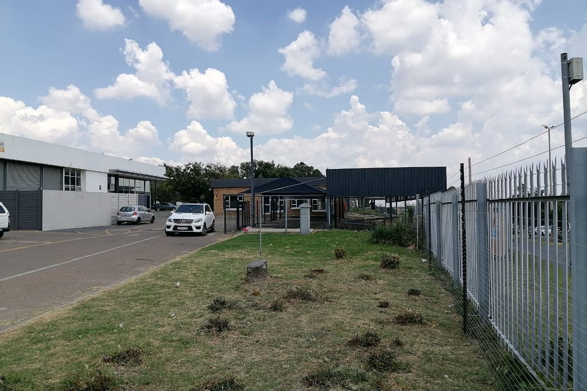 Front exterior view of the commercial property featuring a paved driveway, security fencing, and open lawn area.