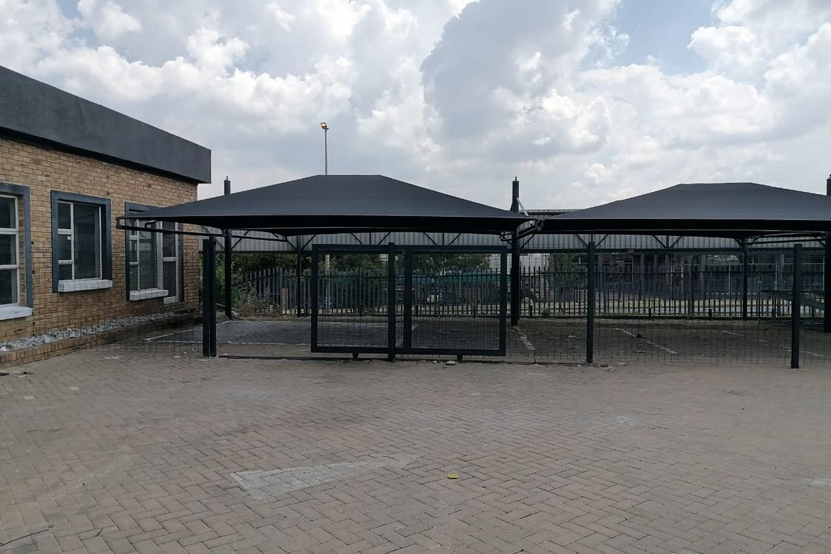 Commercial exterior area featuring a paved driveway, secure steel fencing with a sliding gate, and covered shade cloth parking bays.