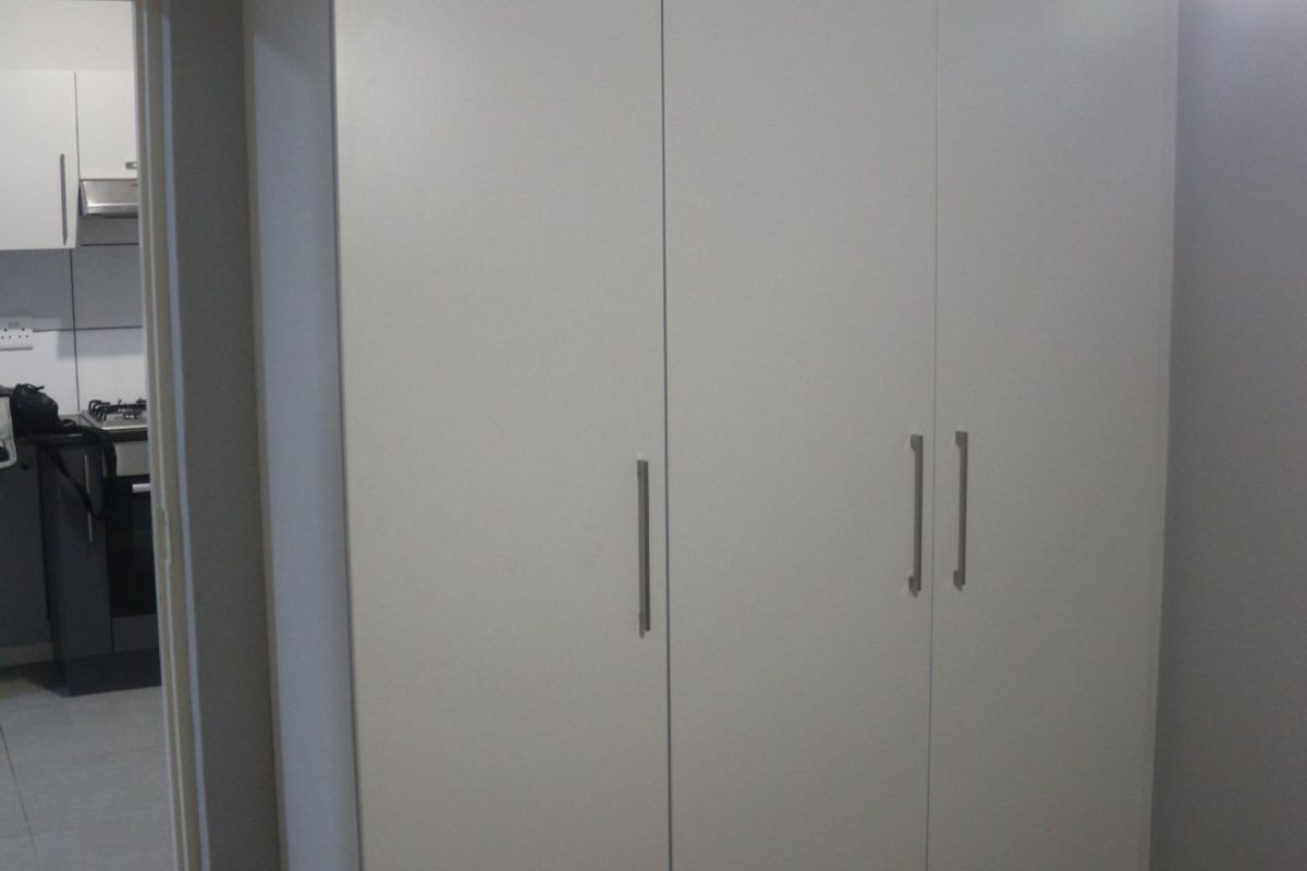 A bedroom featuring a clean, white built-in wardrobe with modern handles, offering ample storage space.