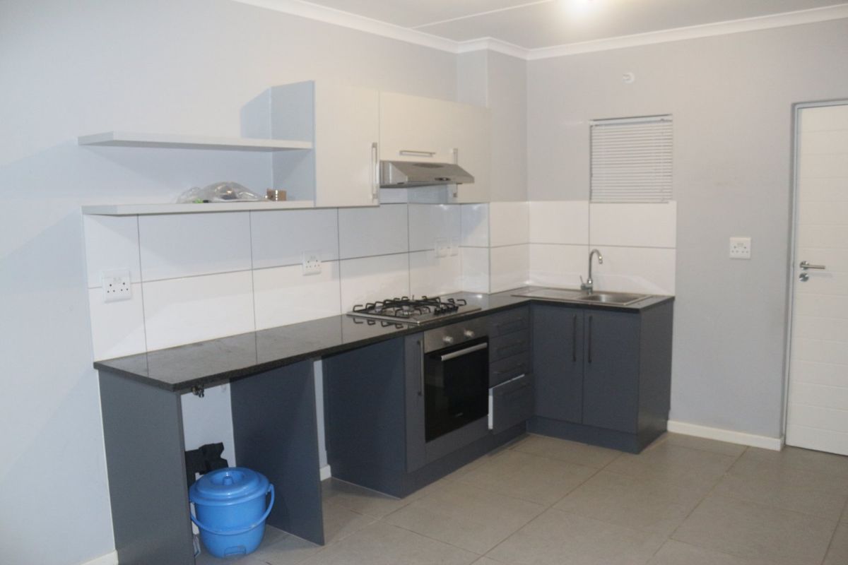 Modern kitchen featuring dark grey cabinetry, granite countertops, built-in oven, gas hob, and tiled splashback in a clean, neutral space.