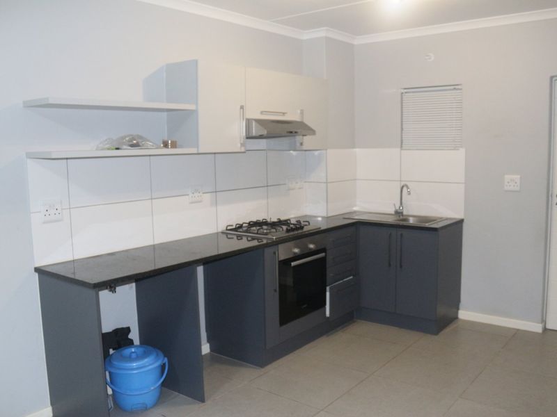 Modern kitchen featuring dark grey cabinetry, granite countertops, built-in oven, gas hob, and tiled splashback in a clean, neutral space.