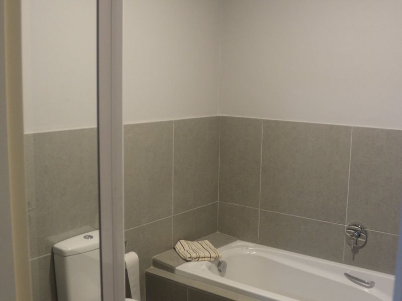 A clean, neutral-toned bathroom featuring a built-in bathtub, tiled surround, and a modern toilet, offering a functional and well-maintained space.