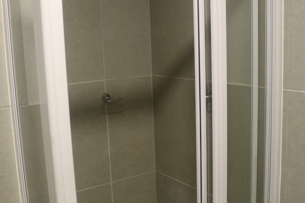 A clean, modern shower stall featuring grey wall tiles, a white tiled floor, and a white-framed glass enclosure.