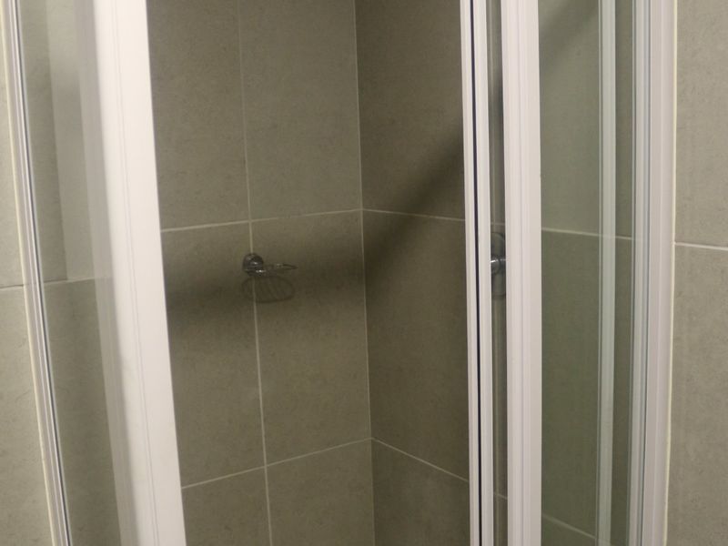 A clean, modern shower stall featuring grey wall tiles, a white tiled floor, and a white-framed glass enclosure.