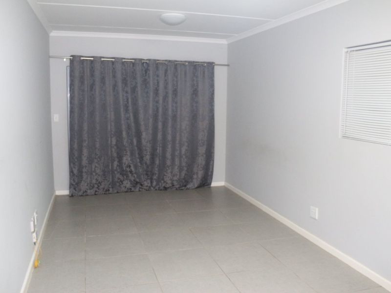 An empty living room featuring neutral tiled flooring, a sliding door with curtains, and a window with venetian blinds.