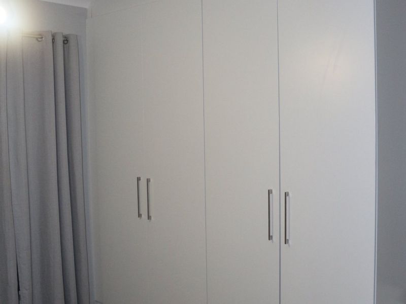 A bedroom featuring a large, modern white built-in wardrobe with sleek handles.