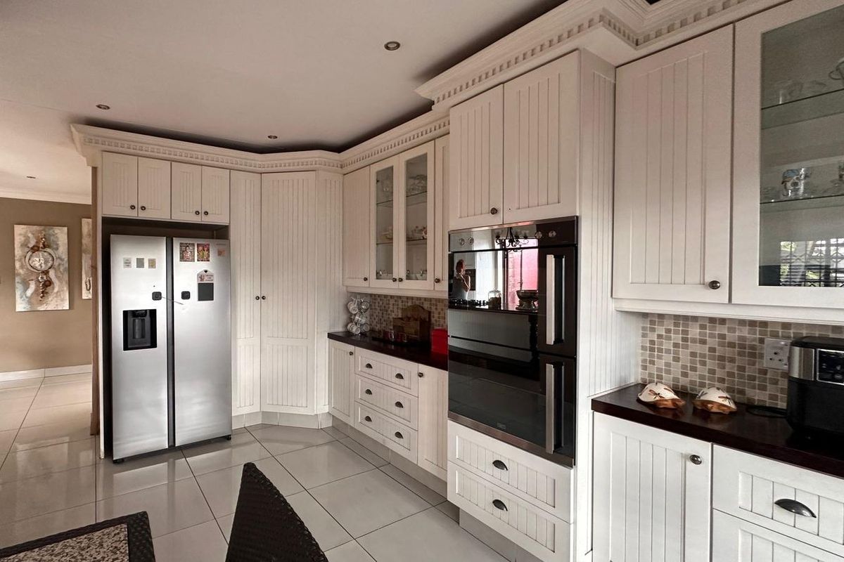 A well-maintained kitchen featuring white paneled cabinetry, dark countertops, mosaic tile backsplash, built-in double oven, and polished floor tiles.