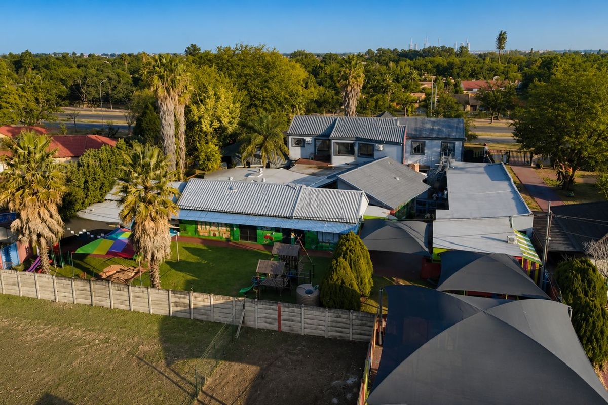 Aerial view of the property featuring multiple connected building structures with corrugated metal roofing, a large garden area, and outdoor shade sail structures.