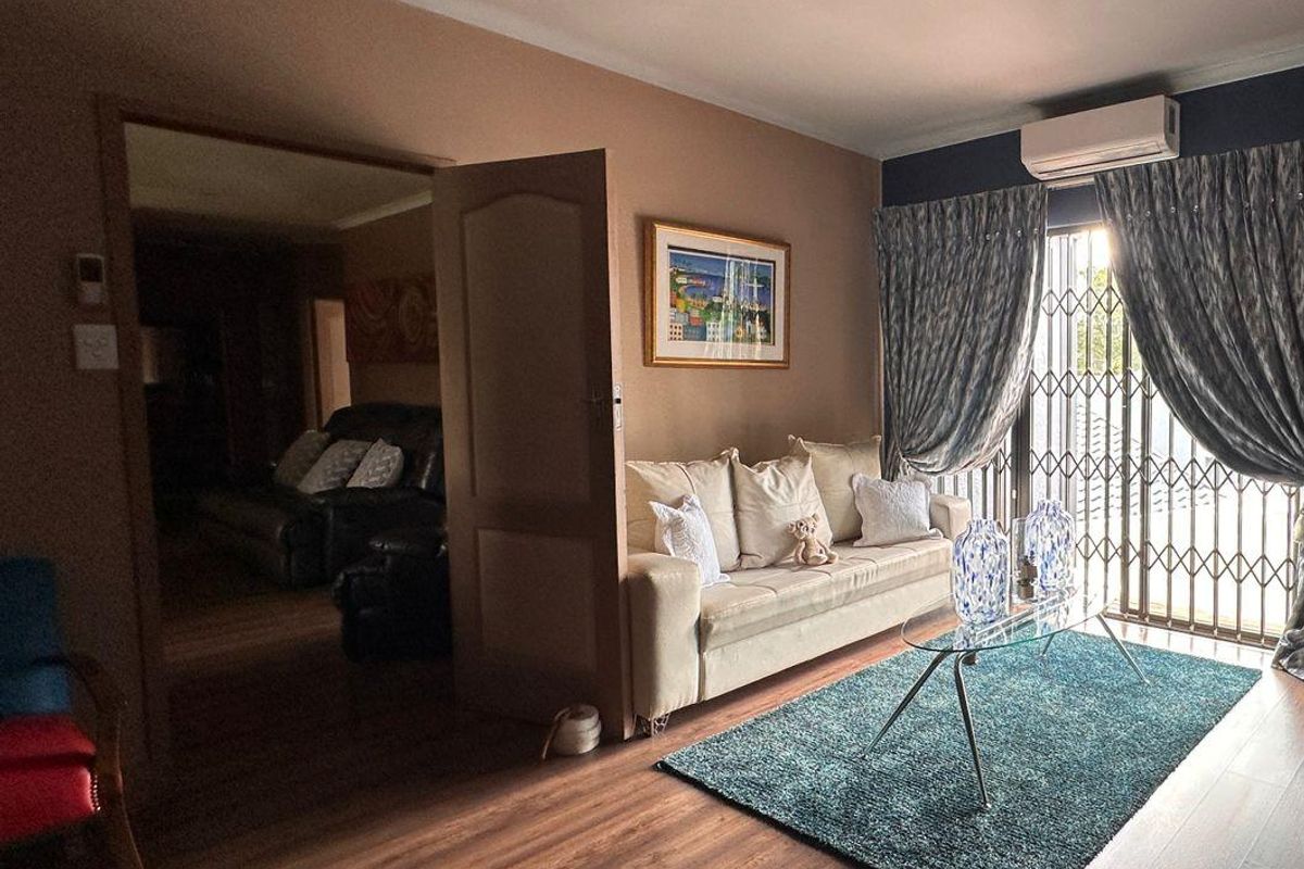 A comfortable living room featuring laminate flooring, a wall-mounted air conditioning unit, and direct access to the exterior through a secure sliding glass door.