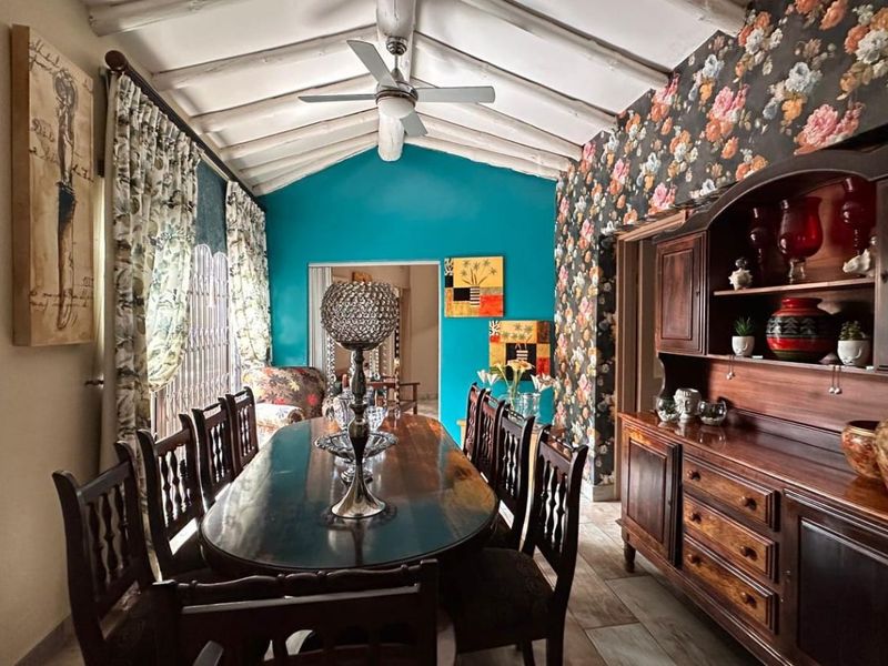A dining room featuring a vaulted ceiling with exposed timber beams, a ceiling fan, and decorative wallpaper.