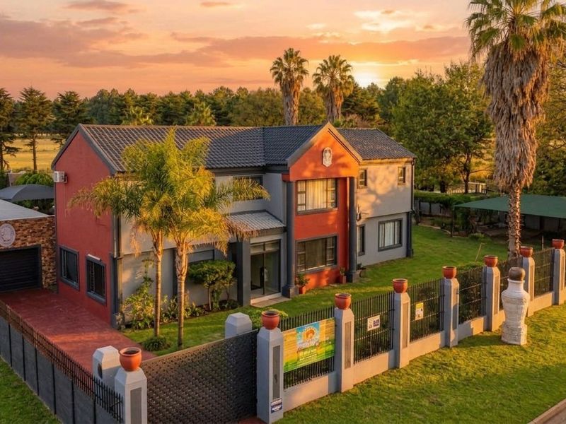 Aerial view of a two-story residential property featuring a tiled roof, perimeter fencing with brick pillars, a paved driveway, and a well-maintained garden.