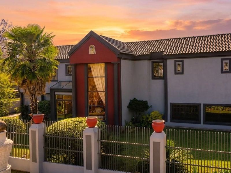 A striking two-story residential facade featuring a bold red architectural accent, large feature window, and secure metal perimeter fencing set within a landscaped garden.