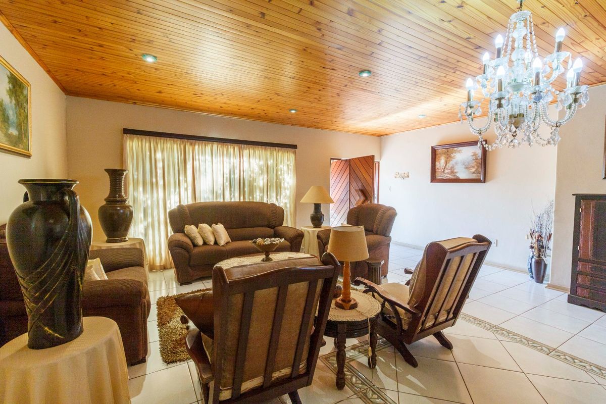 Spacious living room featuring a warm timber tongue and groove ceiling, recessed lighting, a crystal chandelier, and tiled flooring with decorative inlay details.