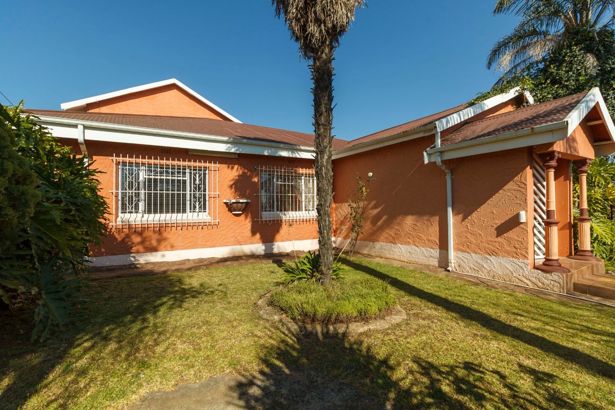 Rear view of the house featuring a textured orange facade, corrugated metal roofing, and security bars on the windows, set against a small garden.