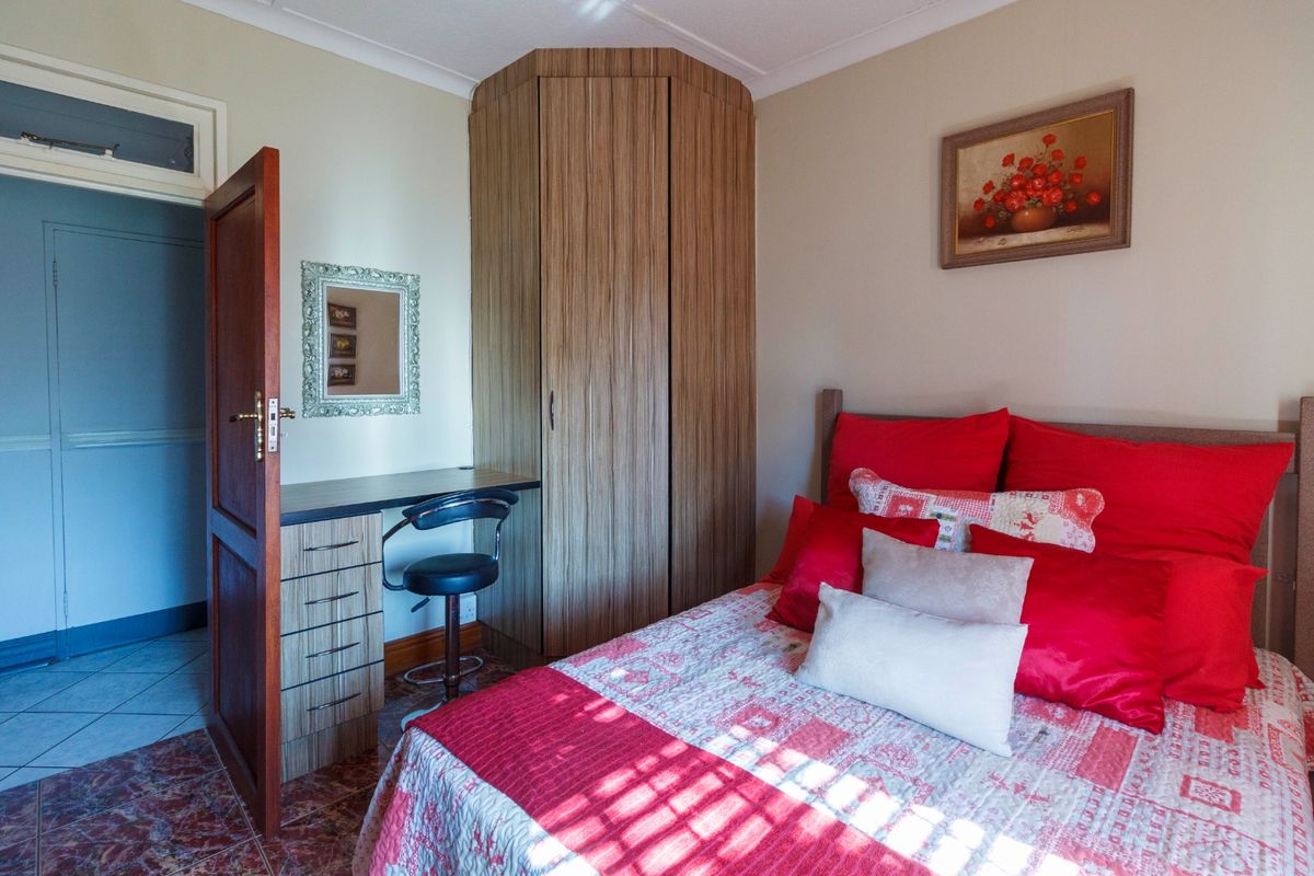 A bedroom featuring built-in cabinetry, including a corner wardrobe and vanity unit, with tiled flooring and neutral wall finishes.