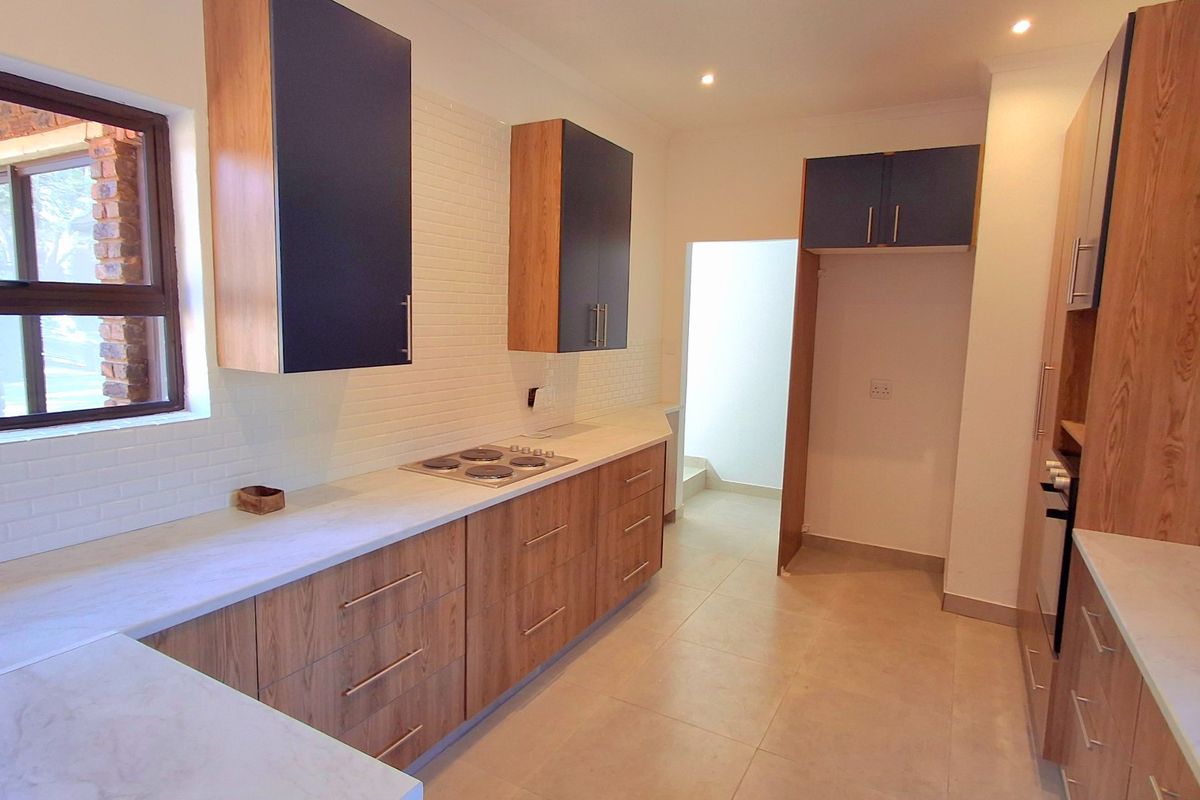 Modern kitchen featuring wood-grain cabinetry, stone countertops, a built-in electric hob, and a clean subway tile backsplash in a bright, open layout.