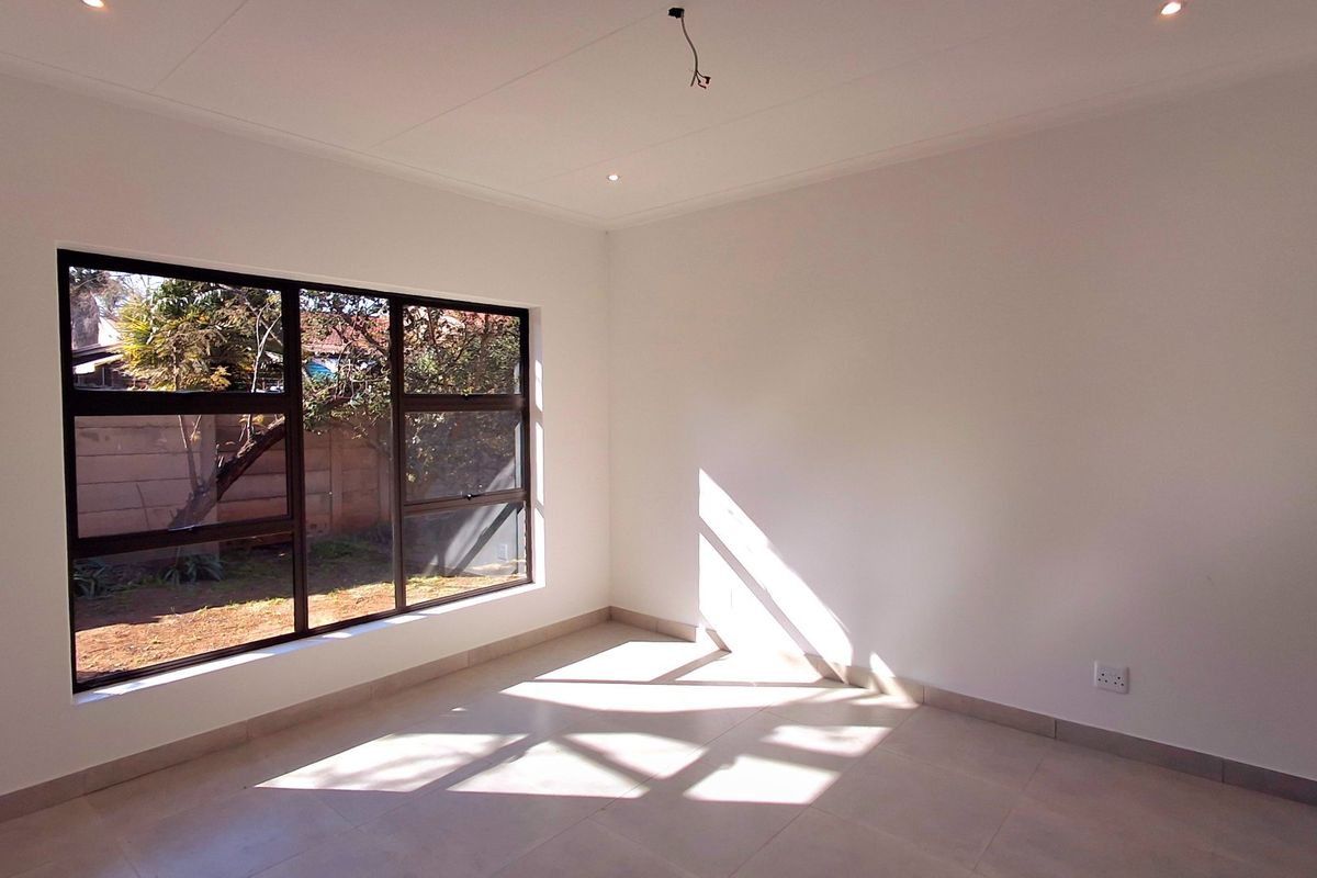 A bright, empty bedroom featuring neutral tiled flooring, large aluminium-framed windows, and recessed lighting, ready for personalization.