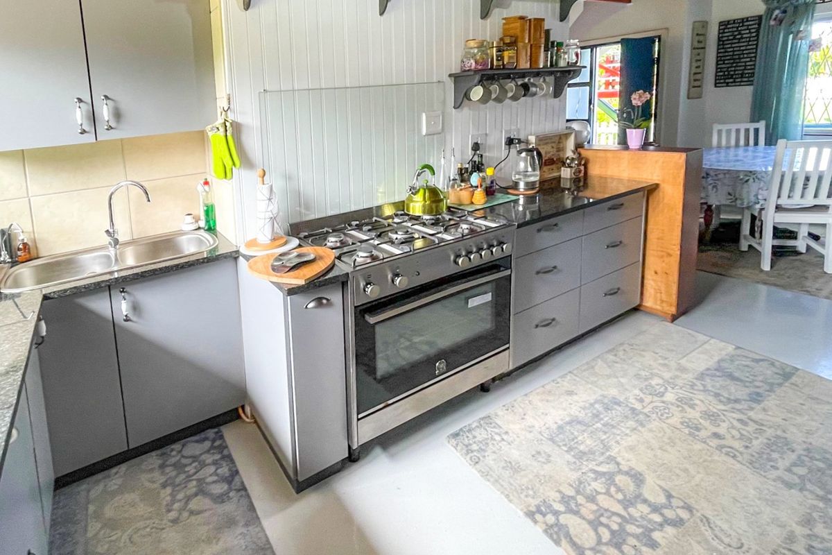 A functional kitchen featuring grey cabinetry, granite countertops, a gas stove with oven, and a stainless steel sink, with an adjacent dining area.