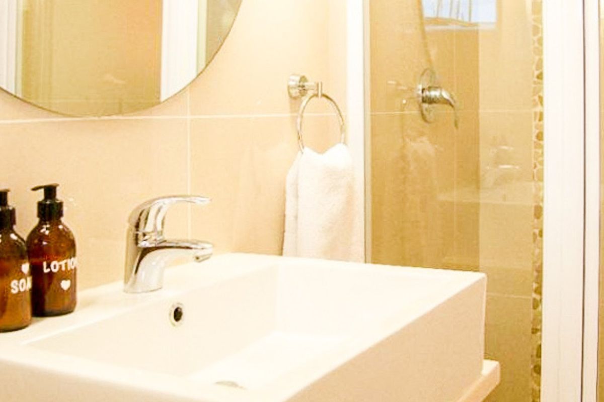 A modern bathroom featuring a clean vessel sink with chrome fixtures, a wall-mounted mirror, and a glass-enclosed shower area with neutral wall tiling.